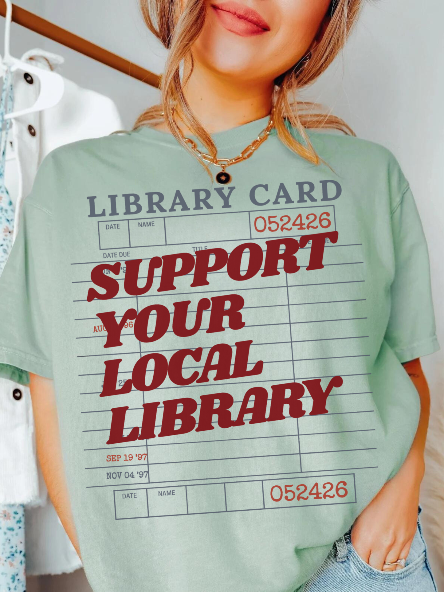woman wearing bay green support your local library graphic t shirt with library card design styled with jeans and layered jewelry