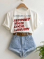 white graphic t shirt styled with denim shorts on hanger featuring vintage library card design with support your local library text