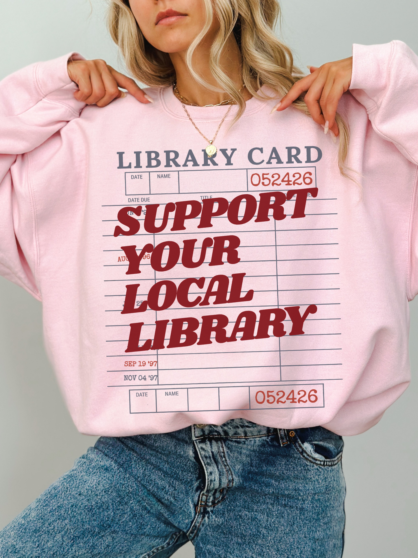 woman wearing pink sweatshirt with support your local library graphic and vintage library card design styled in cozy casual outfit