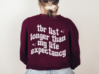 woman in maroon sweatshirt with white bookish graphic that says TBR list longer than my life expectancy
