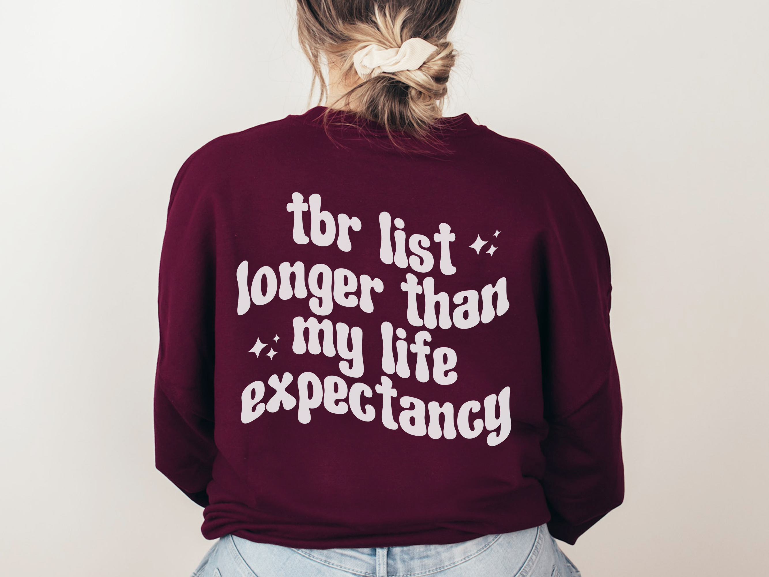 woman in maroon sweatshirt with white bookish graphic that says TBR list longer than my life expectancy