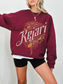 Maroon sweatshirt featuring ornate gold and tan typography reading Kejari Tournament, modeled with black biker shorts and casual layered top, inspired by fantasy book fandom.
