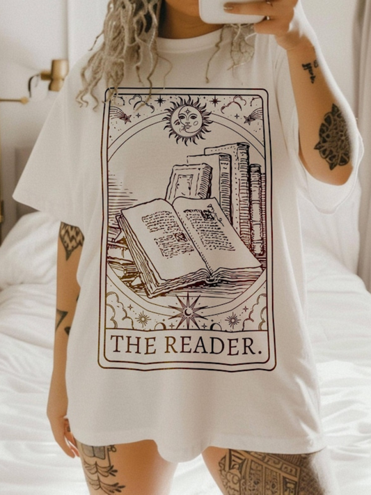 Woman wearing ivory The Reader tarot-style shirt with open book, sun, and bookshelf design, paired with denim shorts
