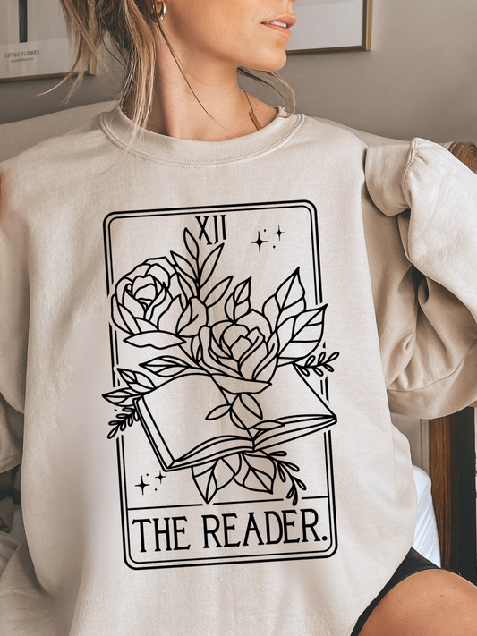 woman lounging in sand The Reader sweatshirt with tarot-style floral book design