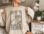 woman in cozy sand-colored sweatshirt featuring hand-drawn tarot card graphic labeled The Writer
