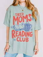 woman wearing bay green tired moms reading club graphic tee with retro reading club typography coffee cup and open book illustration