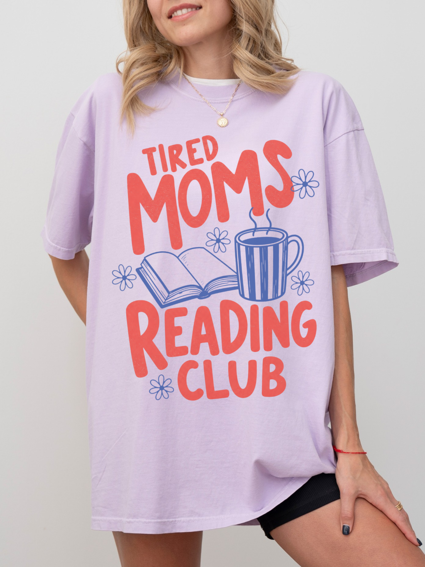 woman wearing oversized orchid tired moms reading club shirt with colorful retro text coffee mug and open book graphic for readers