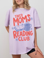 woman wearing oversized orchid tired moms reading club shirt with colorful retro text coffee mug and open book graphic for readers