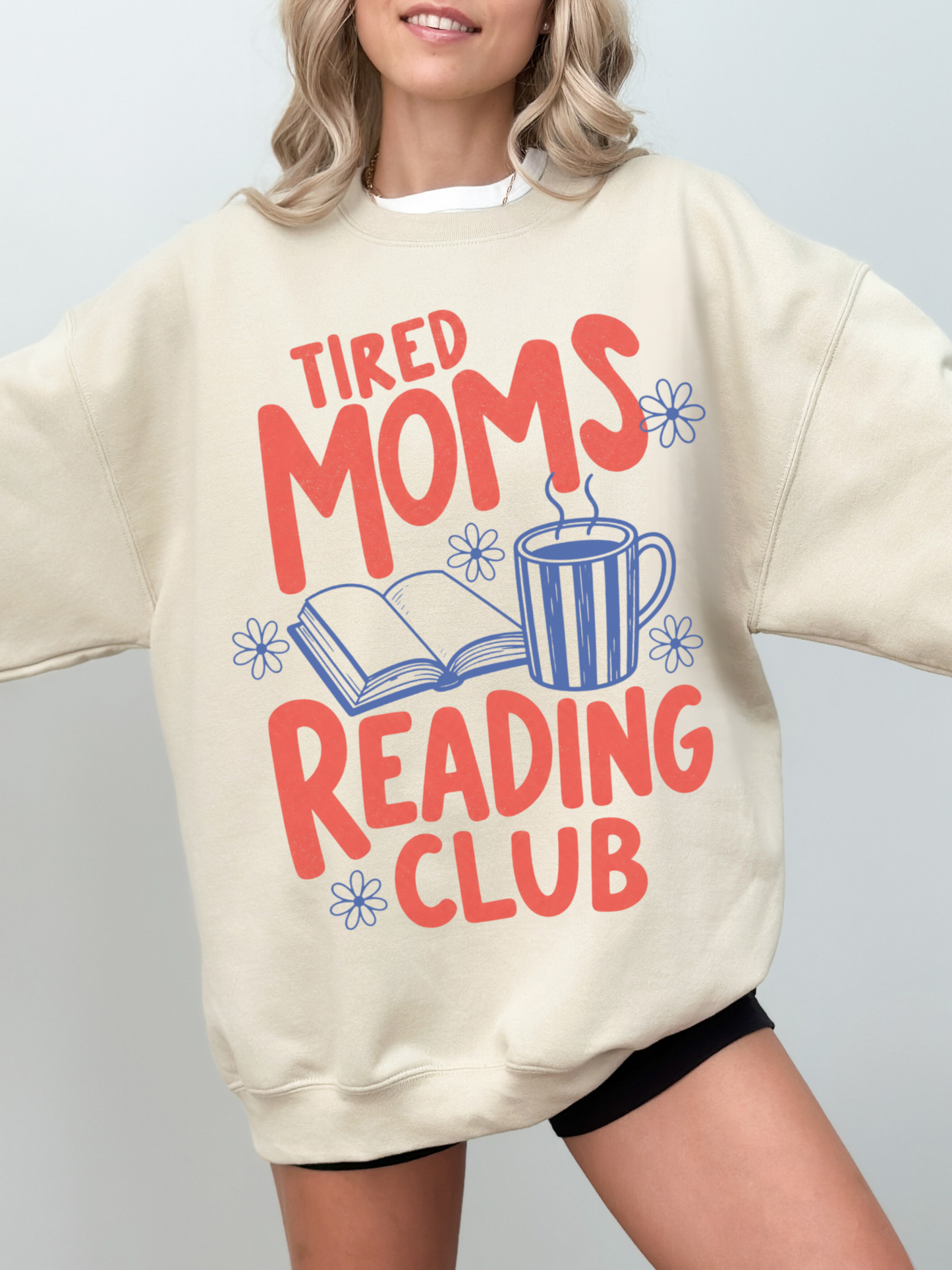 woman wearing oversized sand tired moms reading club sweatshirt with vintage inspired reading club graphic coffee mug and floral doodles