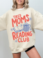 woman wearing oversized sand tired moms reading club sweatshirt with vintage inspired reading club graphic coffee mug and floral doodles
