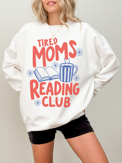 woman wearing oversized white tired moms reading club sweatshirt with retro reading graphic featuring coffee mug open book and floral accents