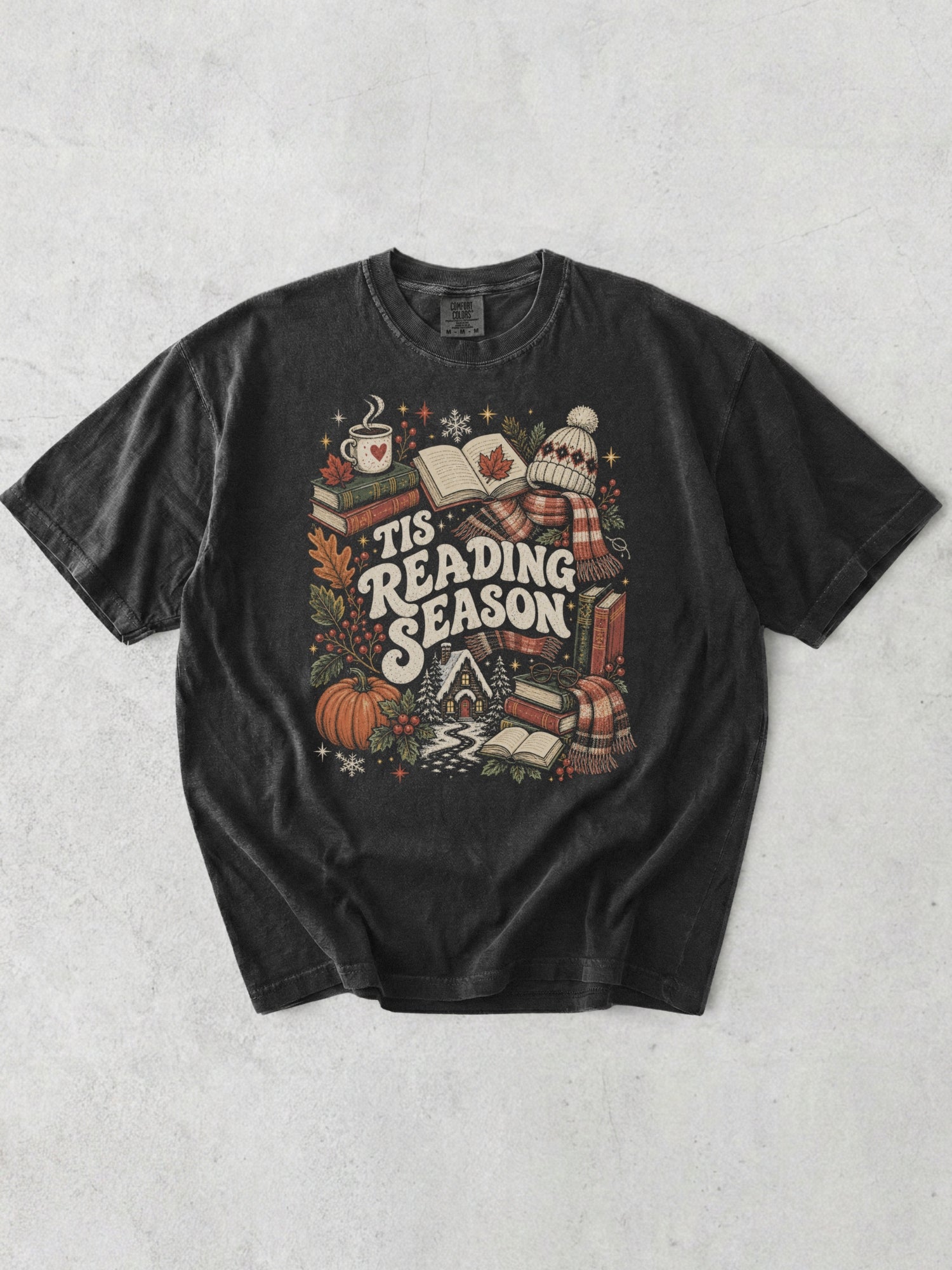 Graphite Comfort Colors shirt featuring a Tis Reading Season design with books, open book, coffee mug, pumpkin, autumn leaves, winter scarf, knit hat and cozy cottage, seasonal bookish t shirt for readers.