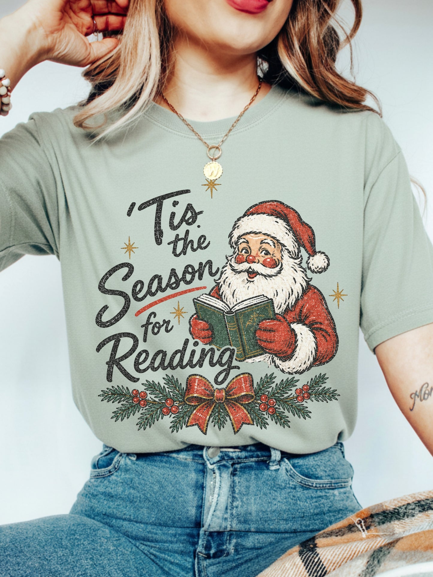 Bay Comfort Colors shirt featuring a vintage Santa reading a book with Tis the Season for Reading text, evergreen branches, red berries, Christmas bow and gold stars, festive bookish Christmas shirt for readers