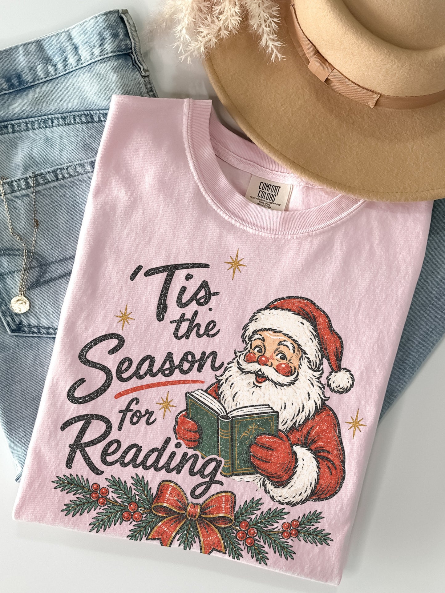Blossom Comfort Colors shirt featuring a vintage Santa reading a green book with Tis the Season for Reading text, evergreen branches, red berries, festive bow and gold stars, Christmas book lover shirt