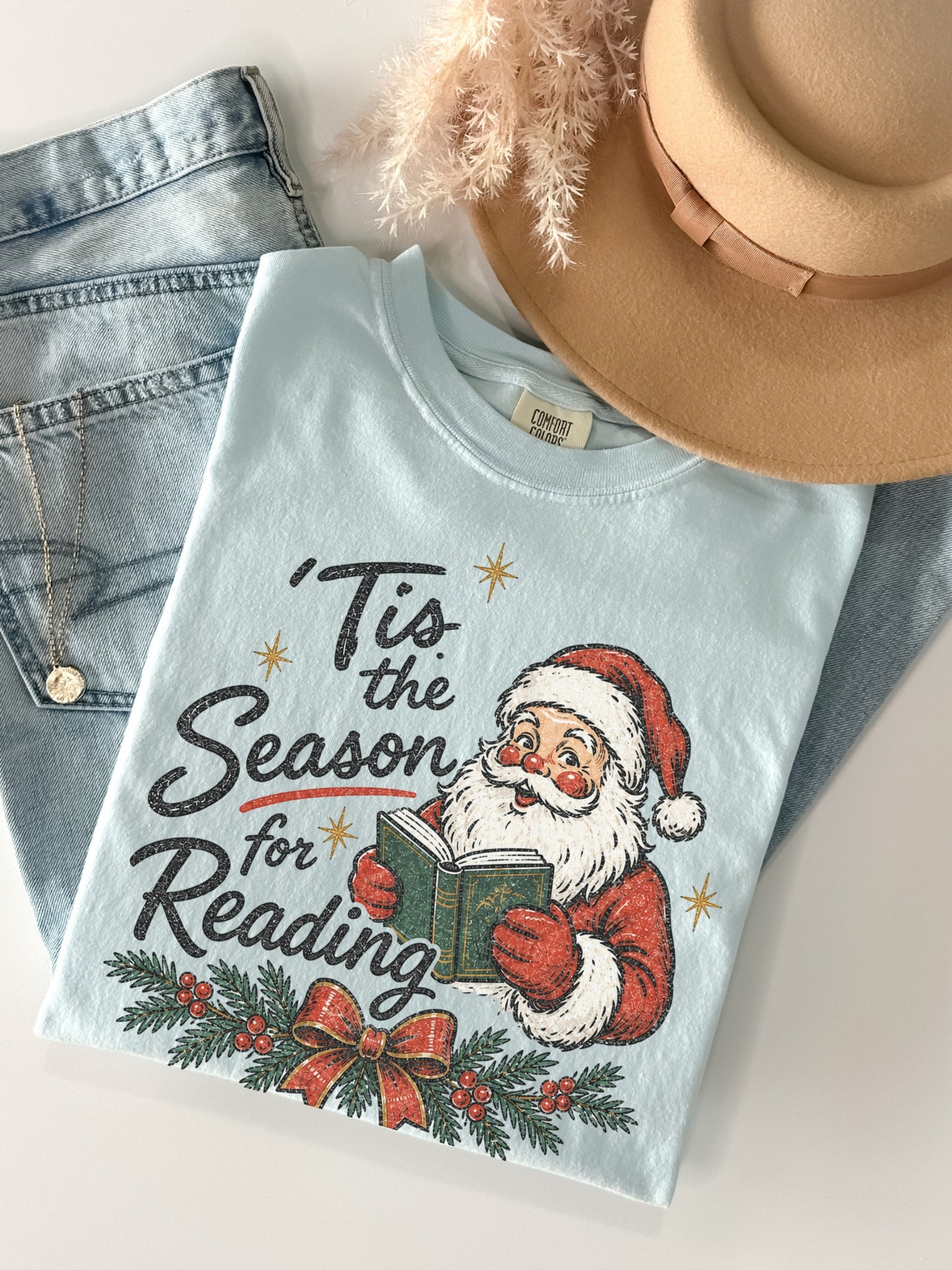 Chambray Comfort Colors shirt featuring a vintage Santa reading a green book with Tis the Season for Reading text, Christmas greenery, red berries, festive bow and gold stars, bookish holiday shirt
