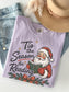 Orchid Comfort Colors shirt featuring a vintage Santa reading a book with Tis the Season for Reading graphic, evergreen branches, red berries, Christmas bow and gold star accents, holiday reading shirt for book lovers