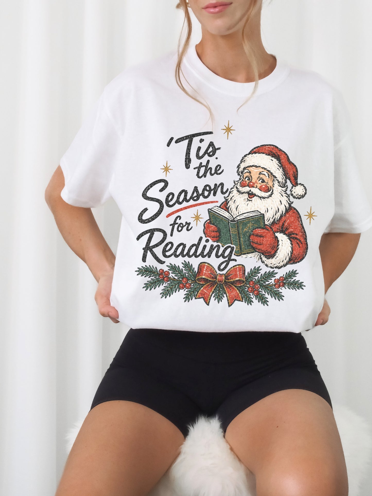 White Comfort Colors shirt modeled with a vintage Santa reading a green book and Tis the Season for Reading text, evergreen branches, red berries, festive bow and gold stars, Christmas reader shirt