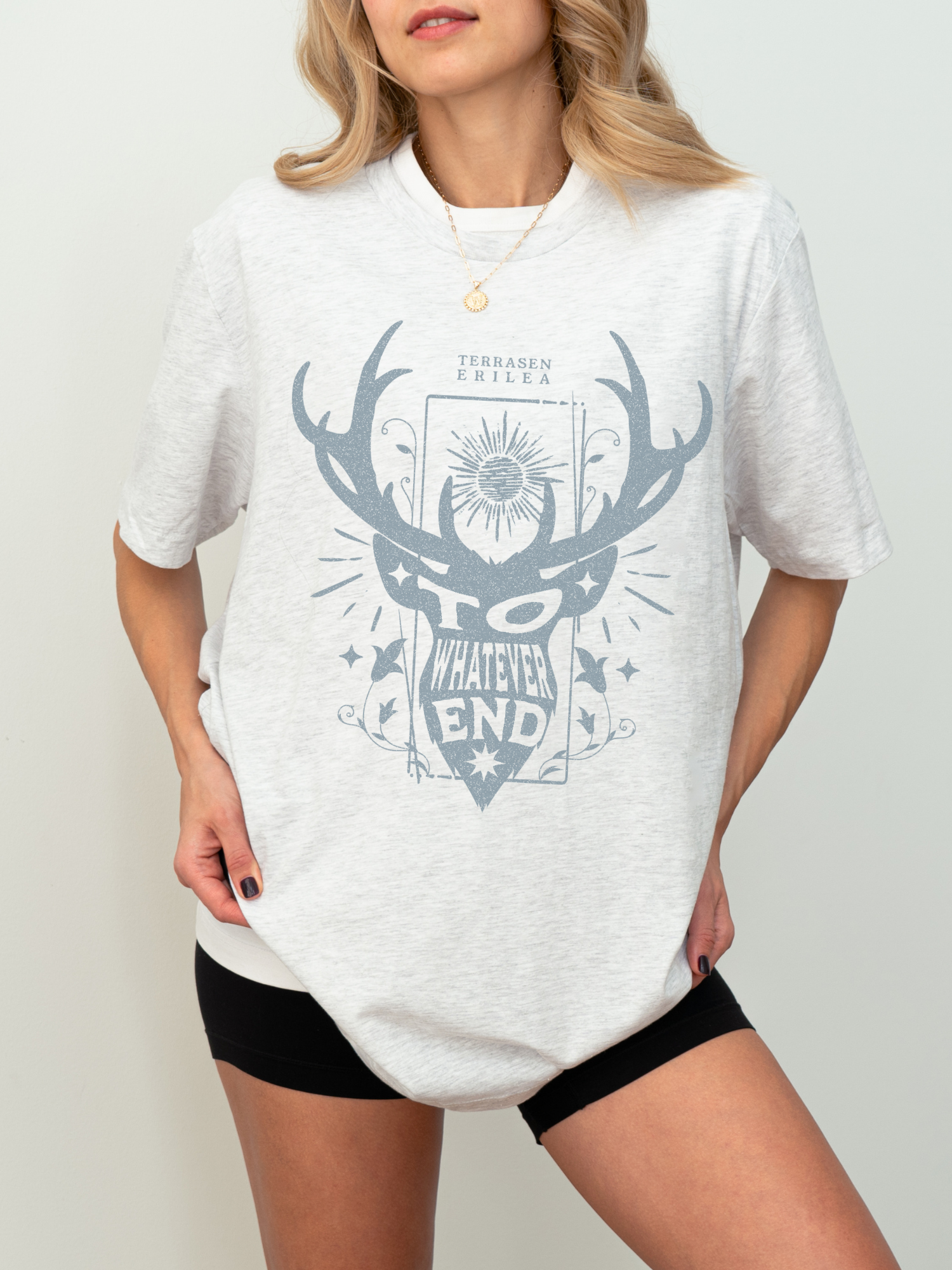 Model in an ash grey “To Whatever End” t-shirt with fantasy bookish design, styled casually with black shorts indoors

