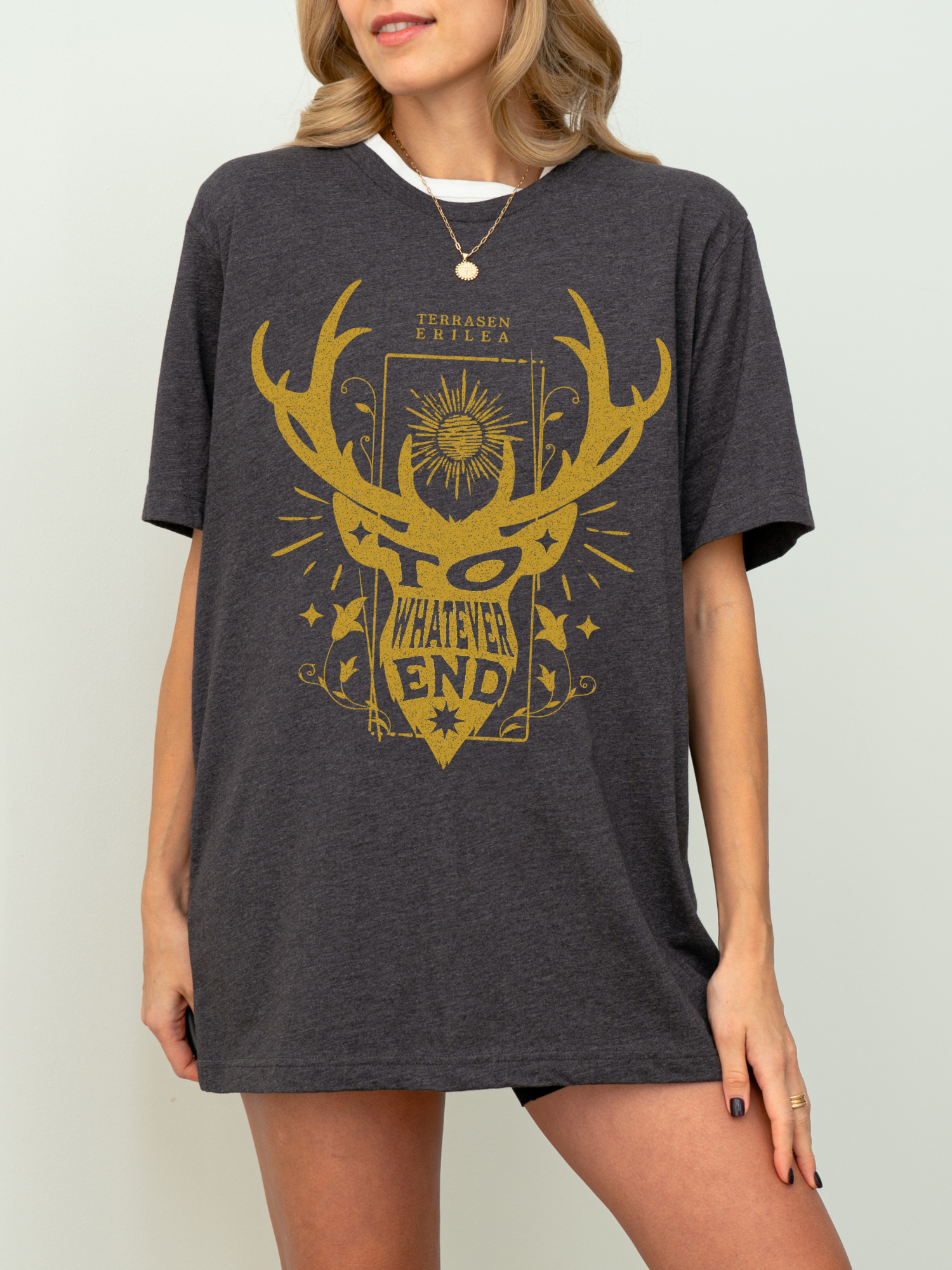 Model in dark heather grey “To Whatever End” t-shirt with fantasy bookish design, styled casually with black shorts indoors


