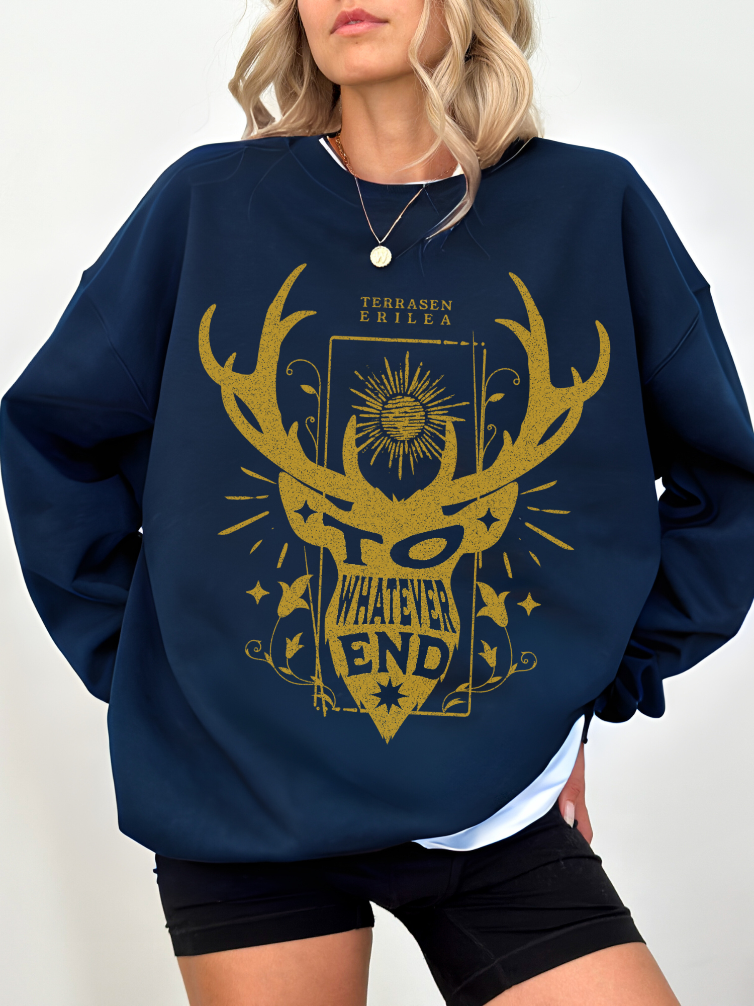 woman wearing navy blue sweatshirt with gold Terrasen crest and the quote “To Whatever End” from Erilea lore

