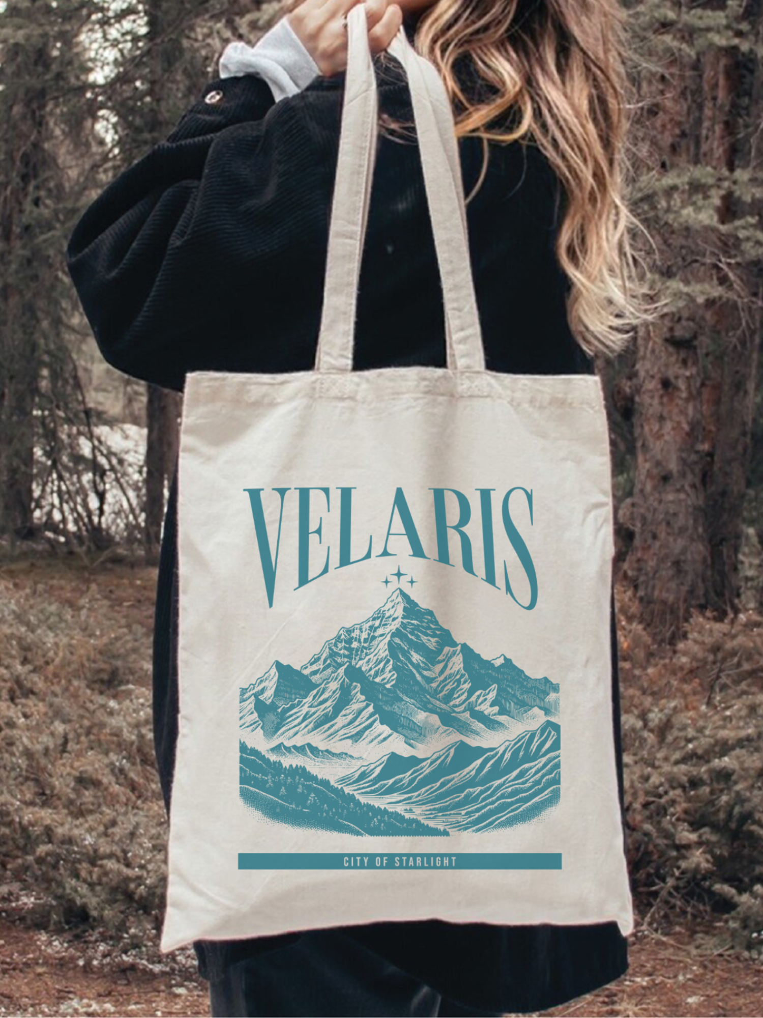 Canvas tote bag featuring a Velaris city of starlight mountain design from a fantasy inspired book theme, worn over the shoulder outdoors in a forest setting. The lifestyle image shows a cozy and adventurous aesthetic, perfect for fantasy readers and book lovers carrying books, groceries, or daily essentials.