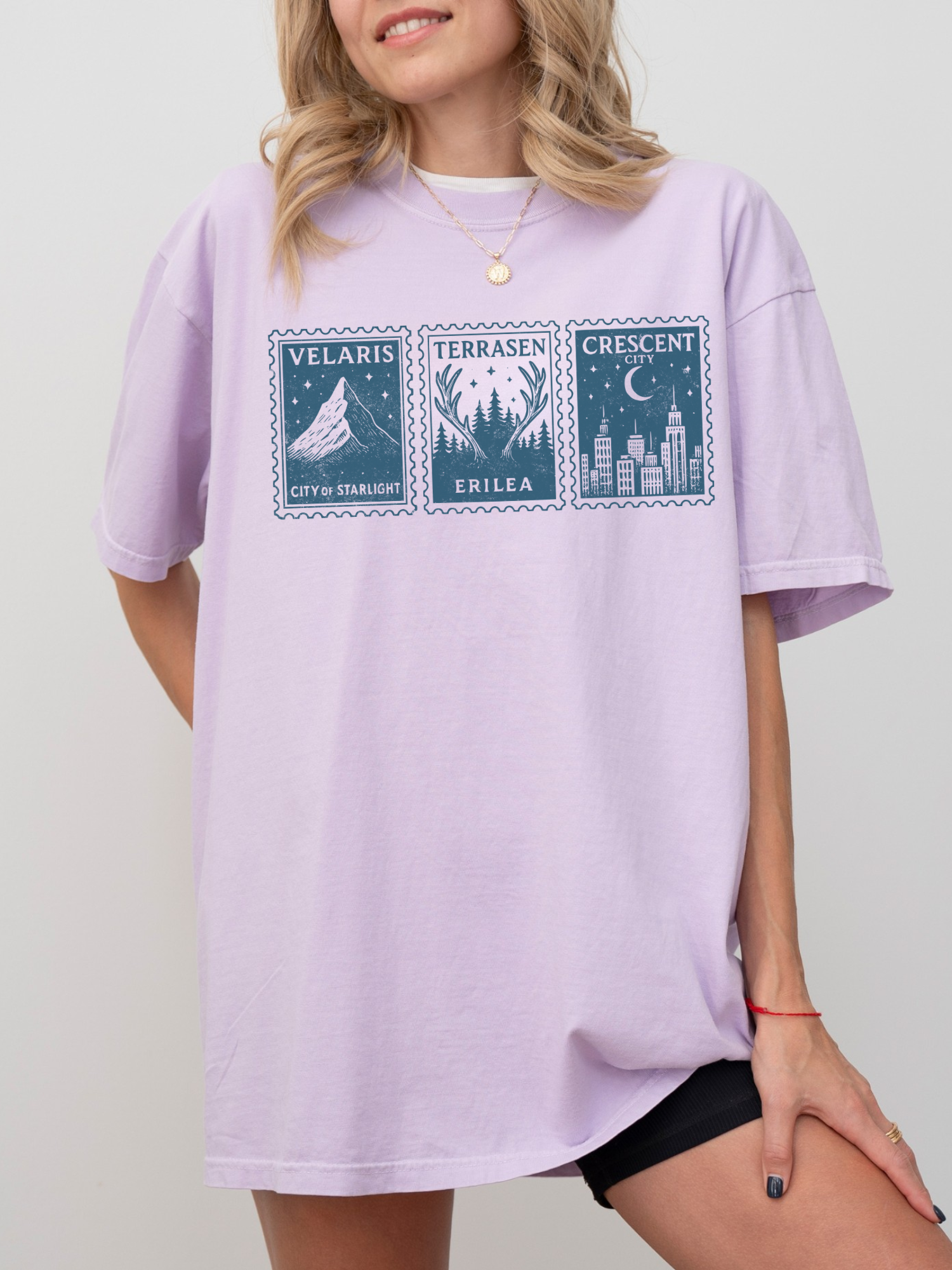 pastel purple oversized t-shirt with Velaris, Terrasen, Crescent City stamps worn by smiling blonde woman