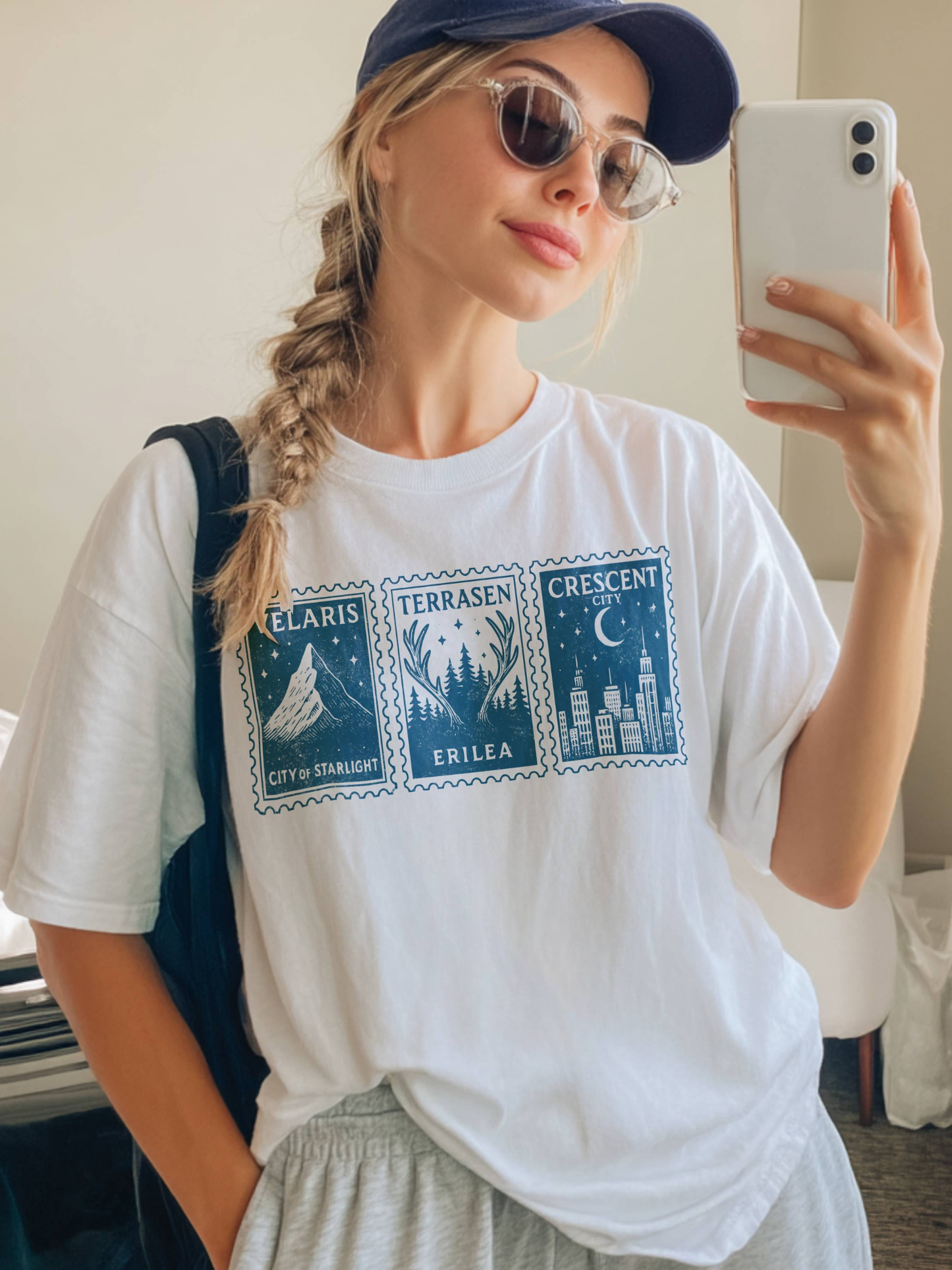 woman in sunglasses and hat taking mirror selfie in white fantasy cities shirt with Velaris Terrasen Crescent City