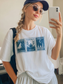 woman in sunglasses and hat taking mirror selfie in white fantasy cities shirt with Velaris Terrasen Crescent City