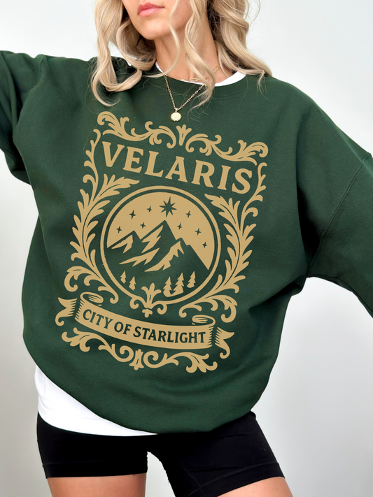 woman in a forest green sweatshirt with magical gold Velaris crest featuring mountains, trees, and stars