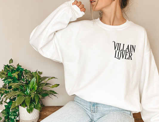 woman wearing white sweatshirt that says villain lover sitting beside green potted plant