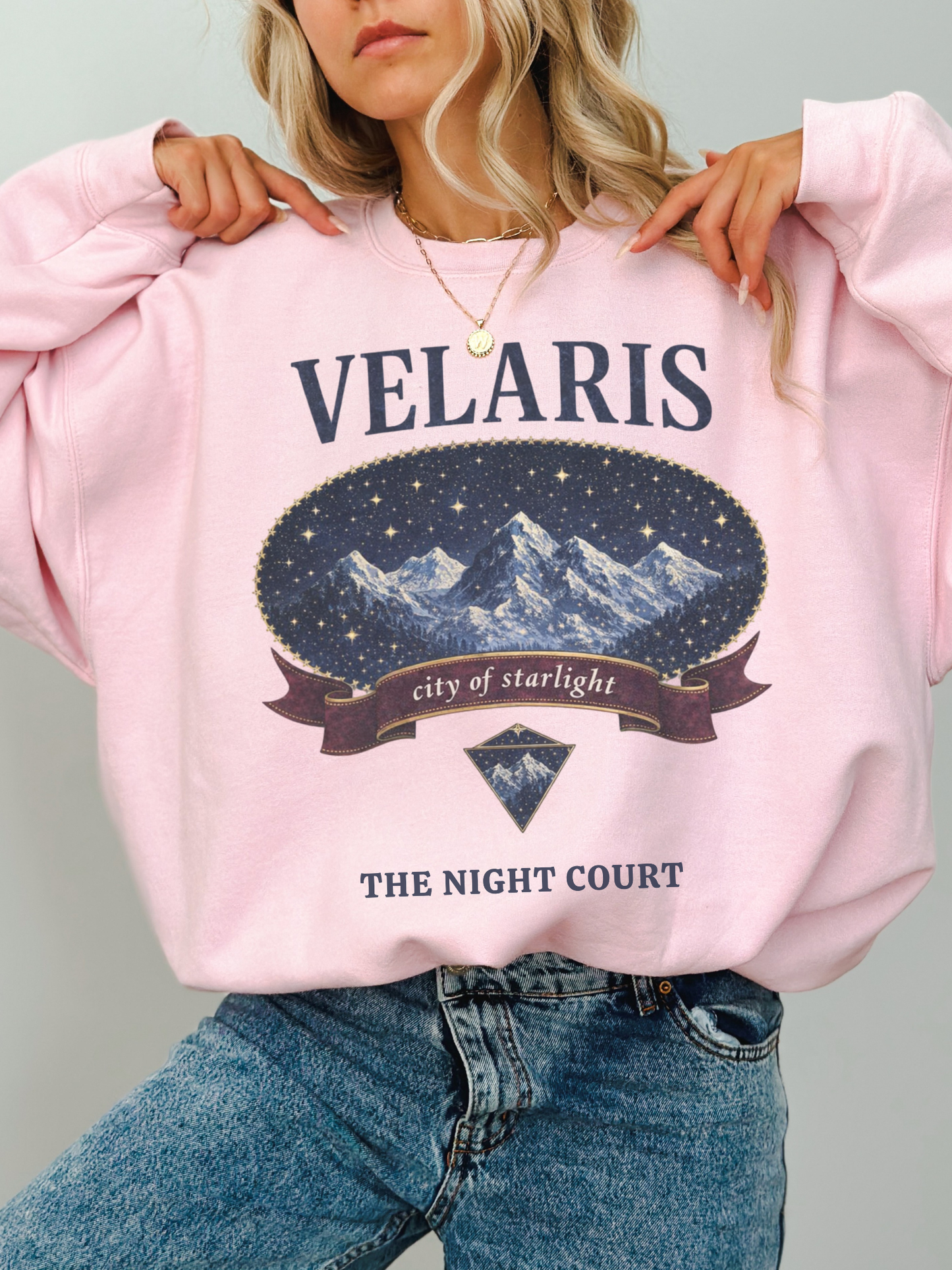 woman wearing a pink vintage velaris sweatshirt with night court inspired mountain illustration