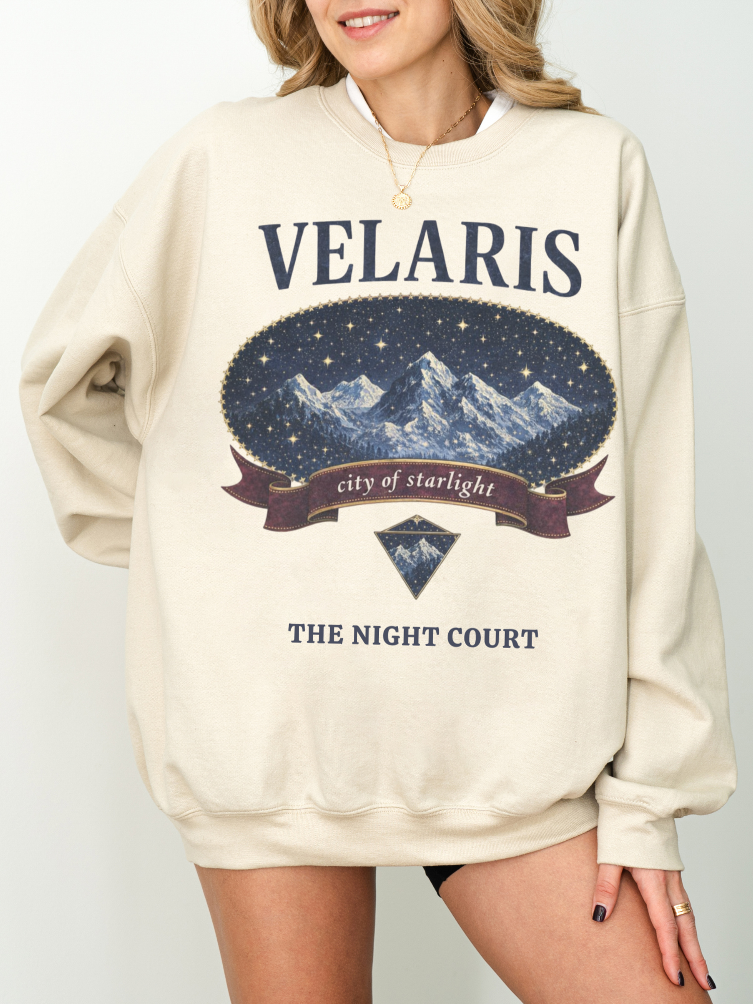 woman wearing a sand colored vintage velaris sweatshirt with celestial night sky and mountain design