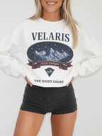 woman wearing a white vintage velaris sweatshirt featuring city of starlight mountain illustration