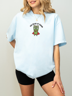woman wearing a chambray Comfort Colors shirt featuring a reading frog holding a book with We Read At Dawn graphic for readers