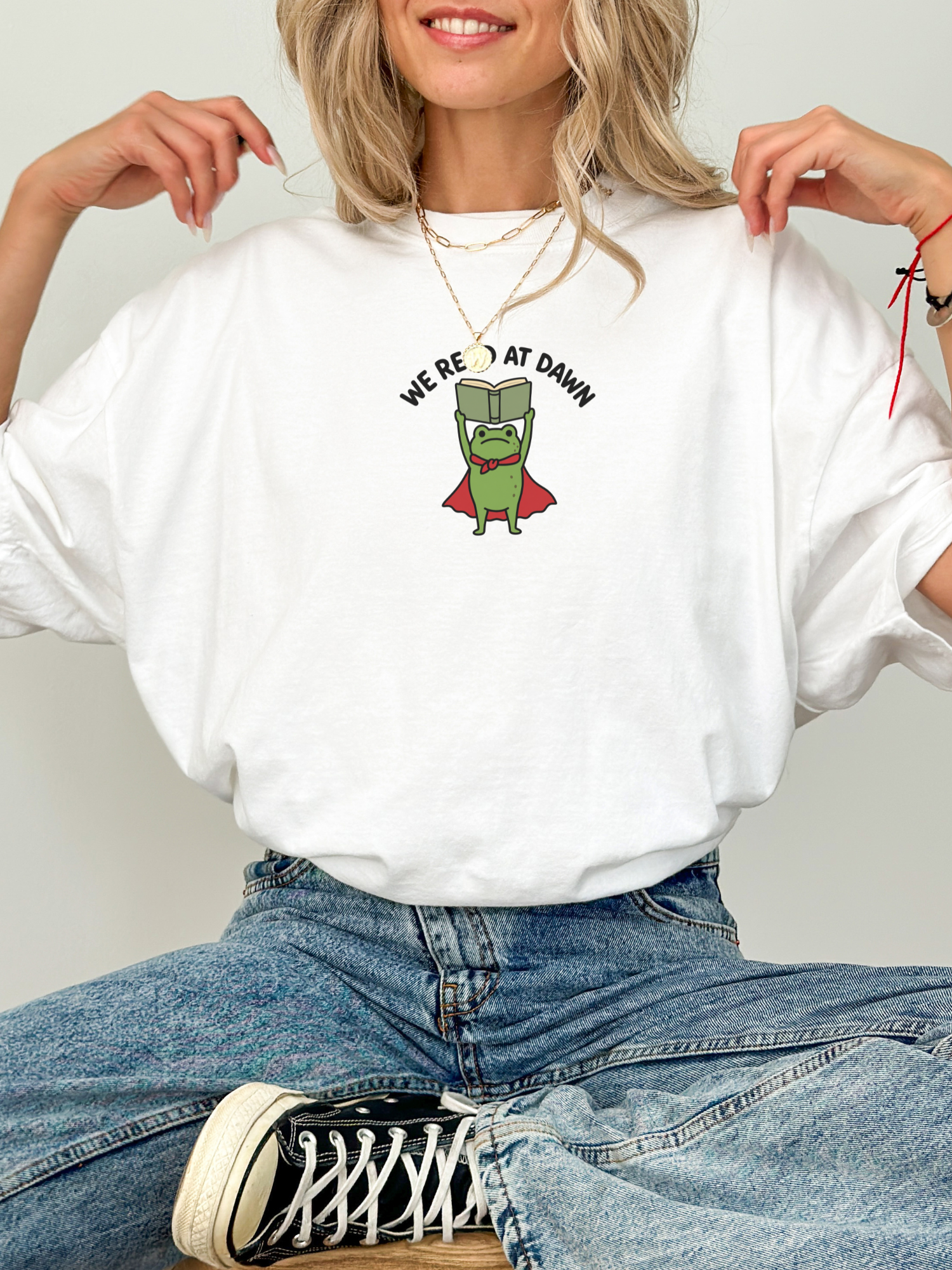 woman wearing a white Comfort Colors shirt featuring a reading frog holding a book with We Read At Dawn graphic for bookworms
