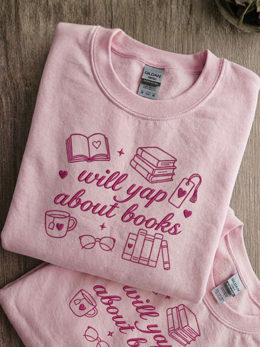 Light pink embroidered sweatshirt with “Will Yap About Books” surrounded by books, hearts, a bookmark, glasses and a tea mug.