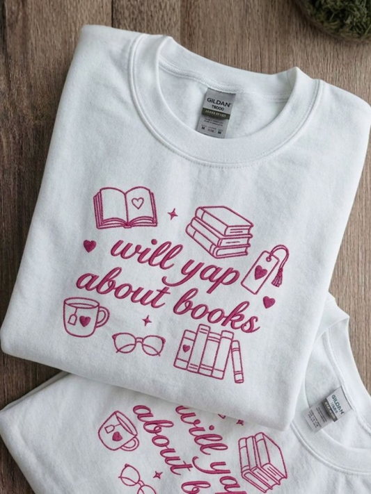 White embroidered book lover sweatshirt featuring “Will Yap About Books” with pink books, hearts, glasses, a bookmark and a tea mug.
