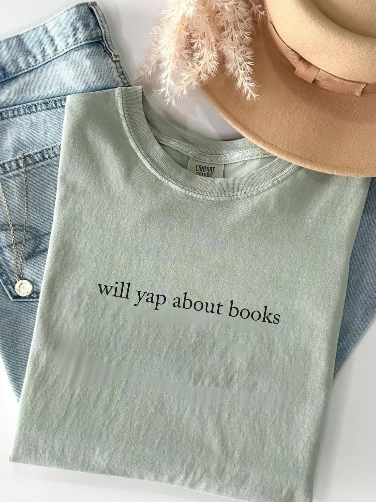 folded bay green t-shirt with black text reading will yap about books styled with hat and denim skirt